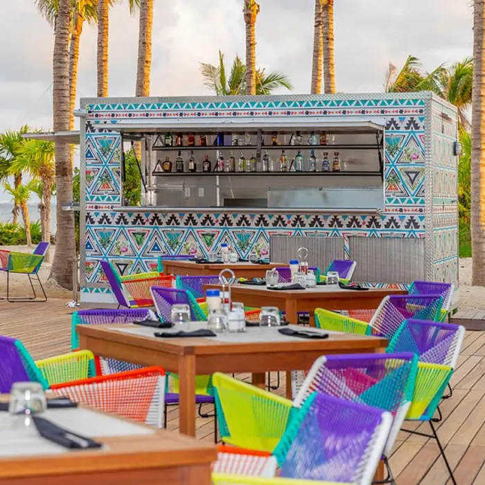 Casual poolside snack bar with turquoise tile decor, shaded seating, and colorful grab-and-go food options.