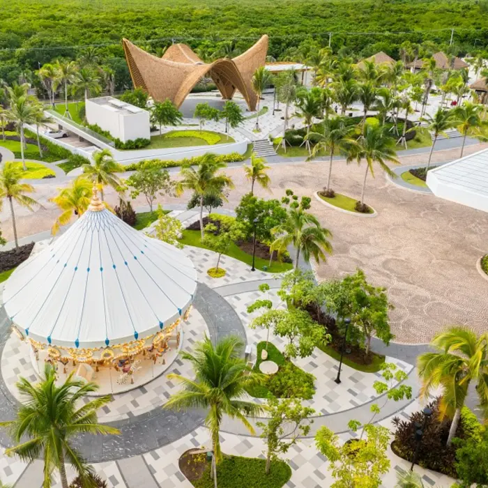 High-angle shot of resort layout with green rooftops, central pools, and beach area opening to blue ocean.