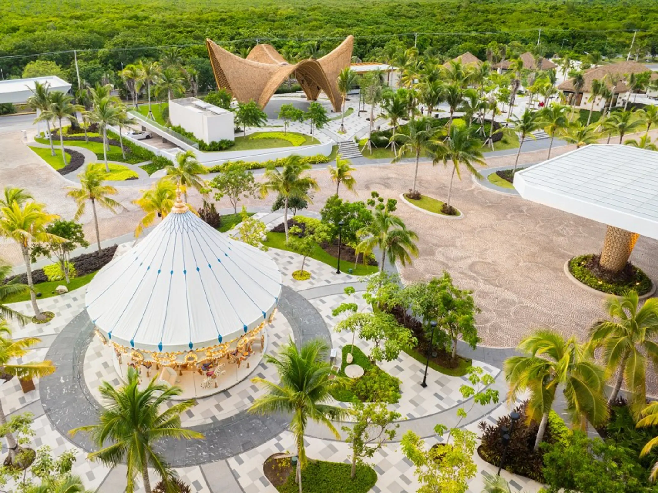 High-angle shot of resort layout with green rooftops, central pools, and beach area opening to blue ocean.