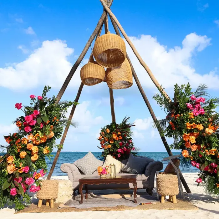 Romantic wedding setup with floral arch, white aisle runner, and oceanfront seating under a glowing sky.