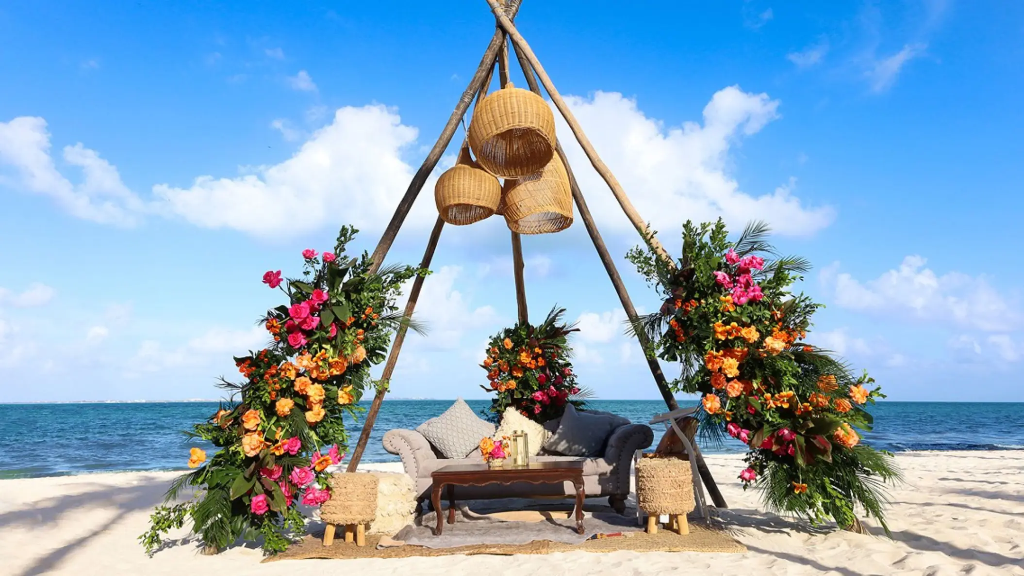 Romantic wedding setup with floral arch, white aisle runner, and oceanfront seating under a glowing sky.