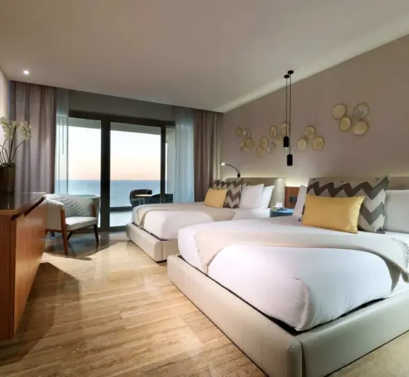 Oceanview guest room with two plush beds, modern lighting, and floor-to-ceiling sliding glass doors.