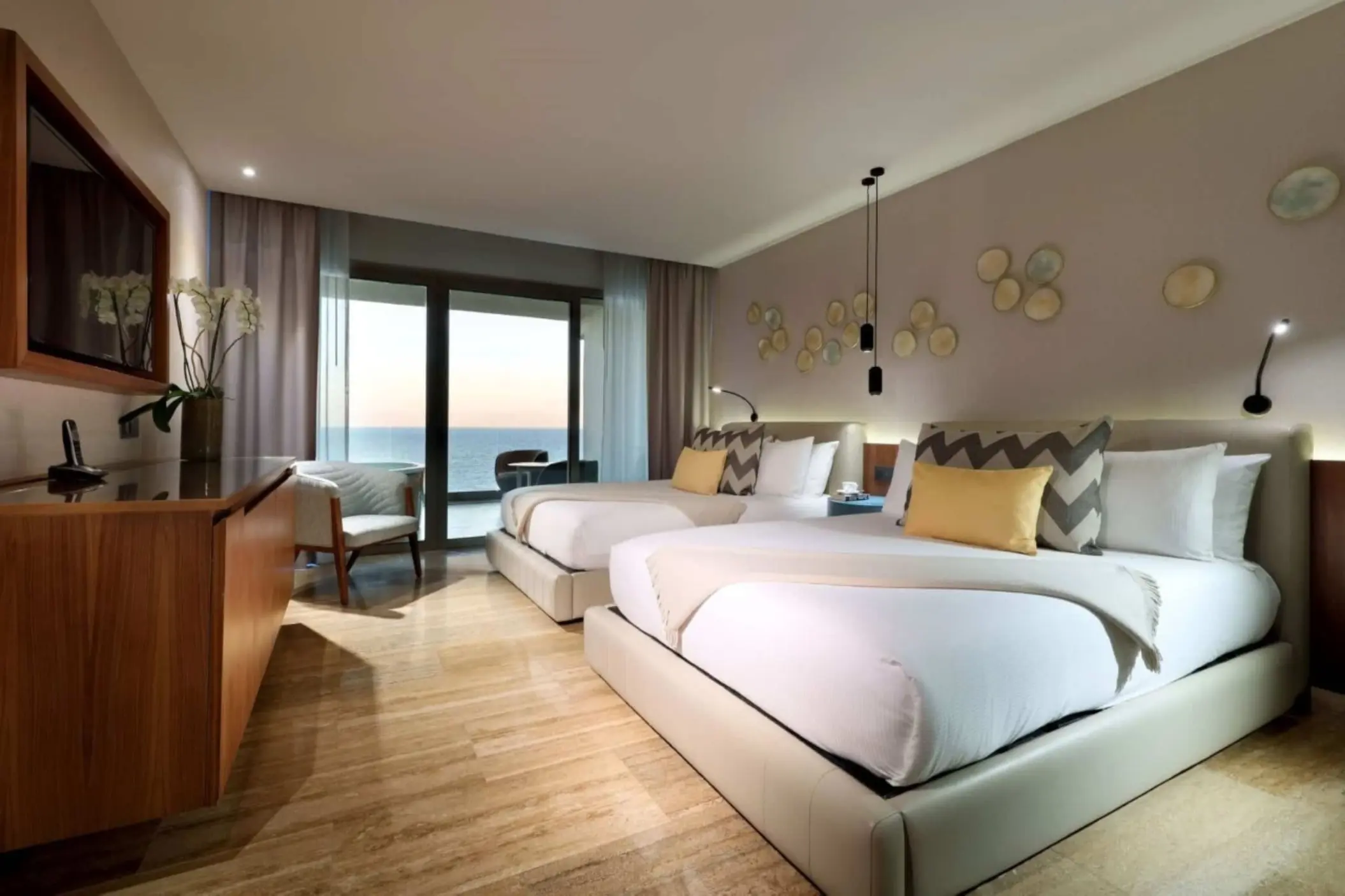 Oceanview guest room with two plush beds, modern lighting, and floor-to-ceiling sliding glass doors.
