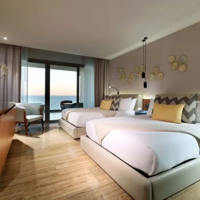 Oceanview guest room with two plush beds, modern lighting, and floor-to-ceiling sliding glass doors.