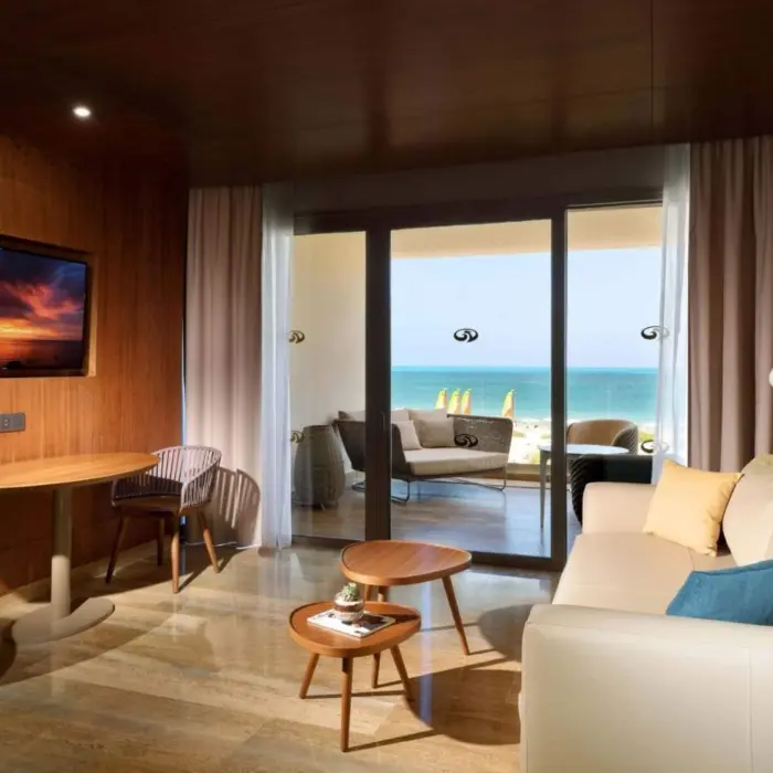 Cozy suite living room with a beach view balcony, warm wood finishes, and modern furniture accents.