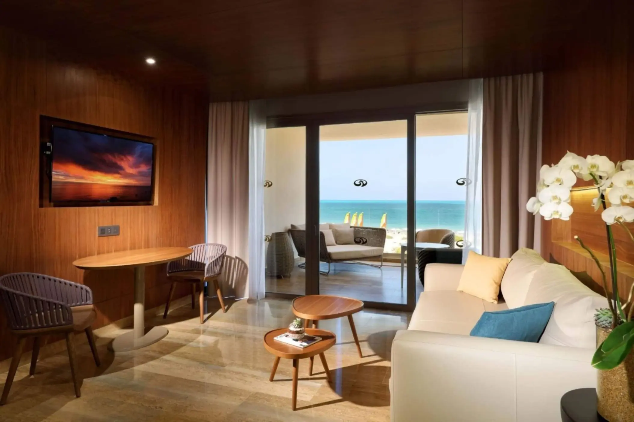 Cozy suite living room with a beach view balcony, warm wood finishes, and modern furniture accents.