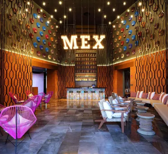Vibrant Mexican-themed lounge bar with colorful chairs and MEX sign wall.
