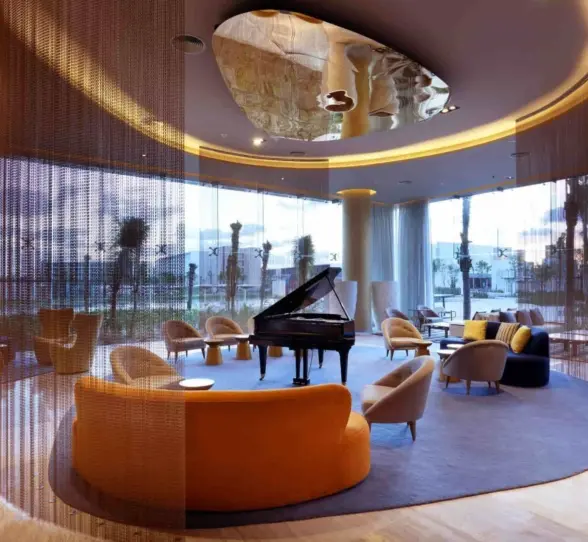 Chic hotel lobby with circular lounge seating, grand piano, and contemporary ceiling design.