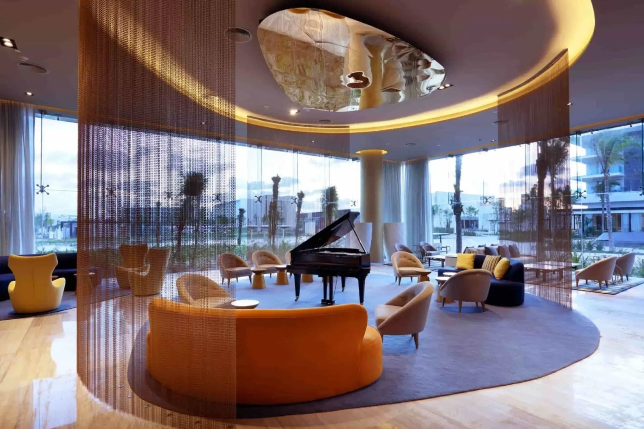 Chic hotel lobby with circular lounge seating, grand piano, and contemporary ceiling design.