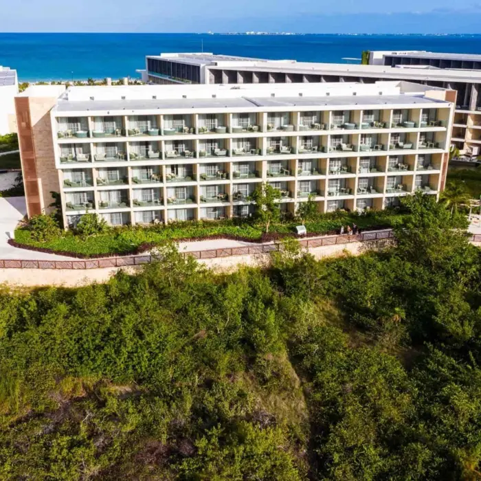 Aerial image of resort buildings surrounded by lush greenery with balconies facing the ocean.