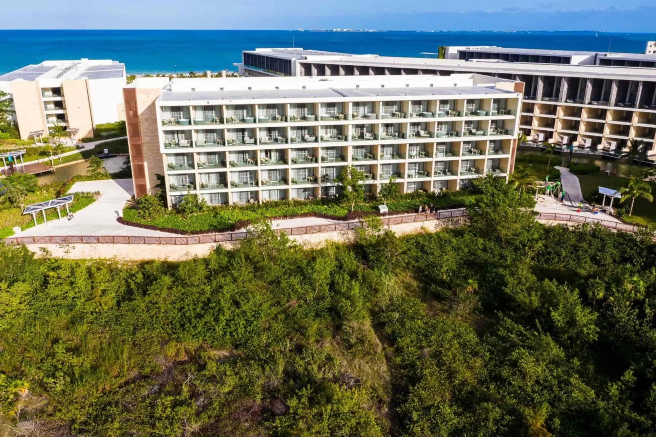 Aerial image of resort buildings surrounded by lush greenery with balconies facing the ocean.