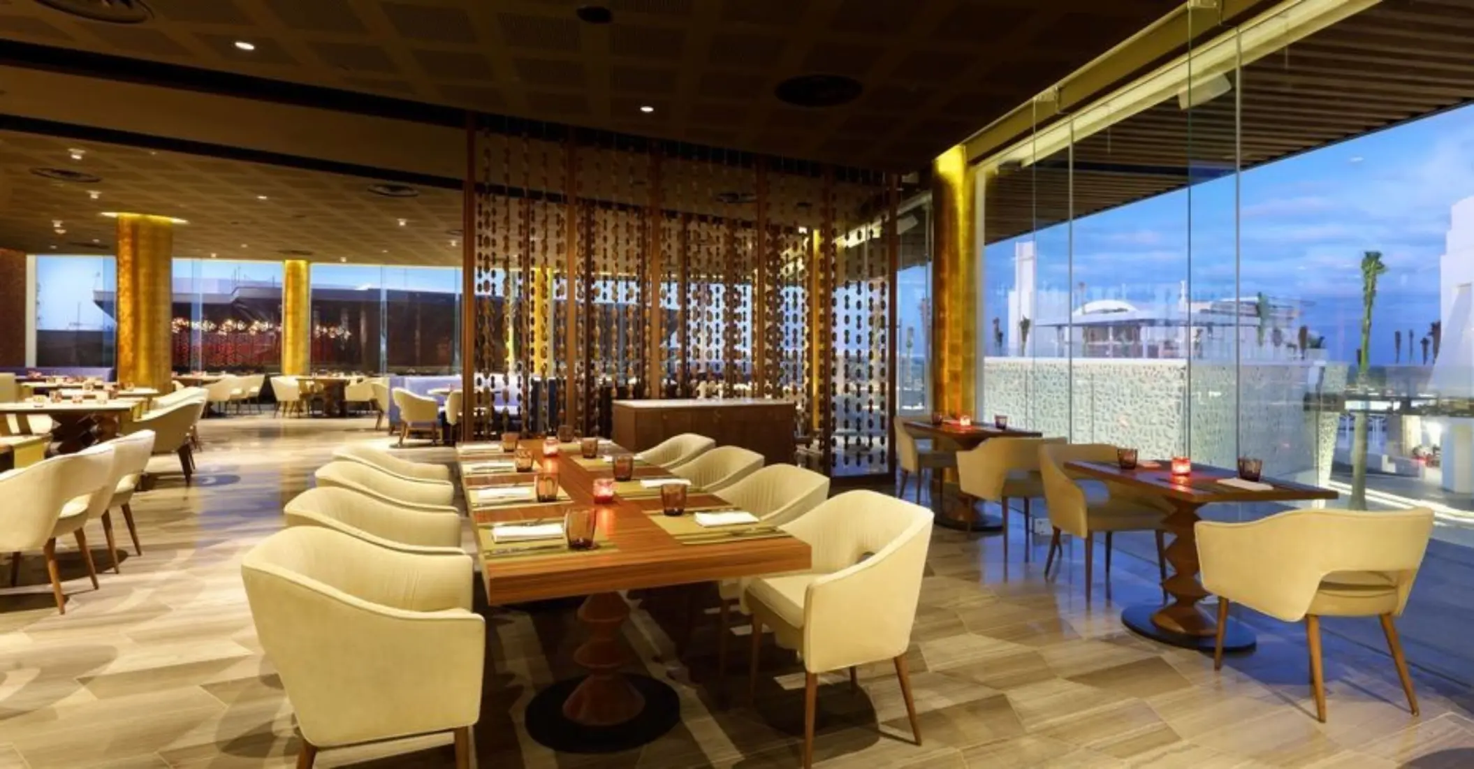 Elegant dining area with cream chairs and warm lighting near large windows at resort restaurant.