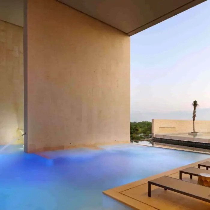 Covered pool with blue lighting surrounded by beige stone walls at luxury resort spa.