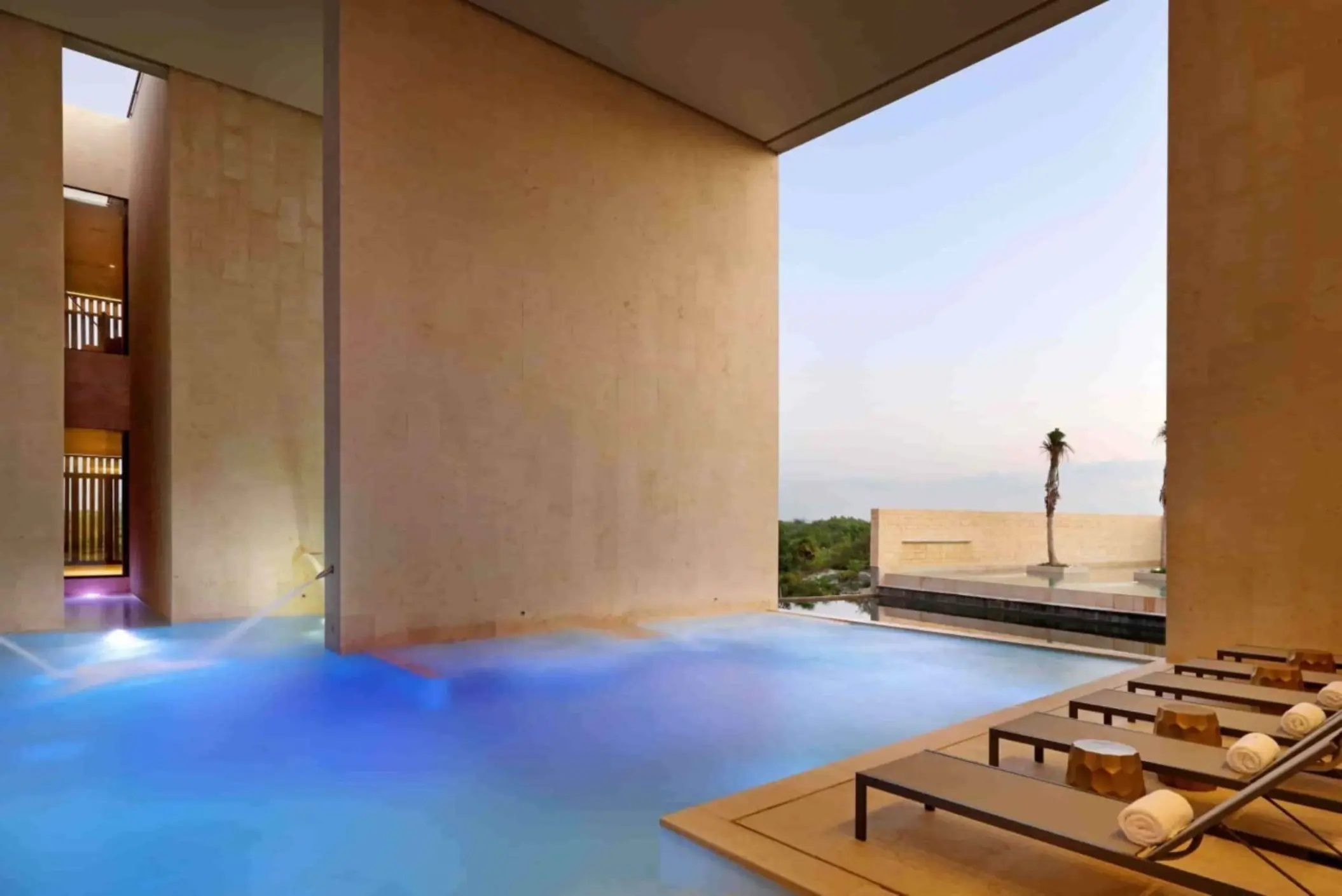 Covered pool with blue lighting surrounded by beige stone walls at luxury resort spa.