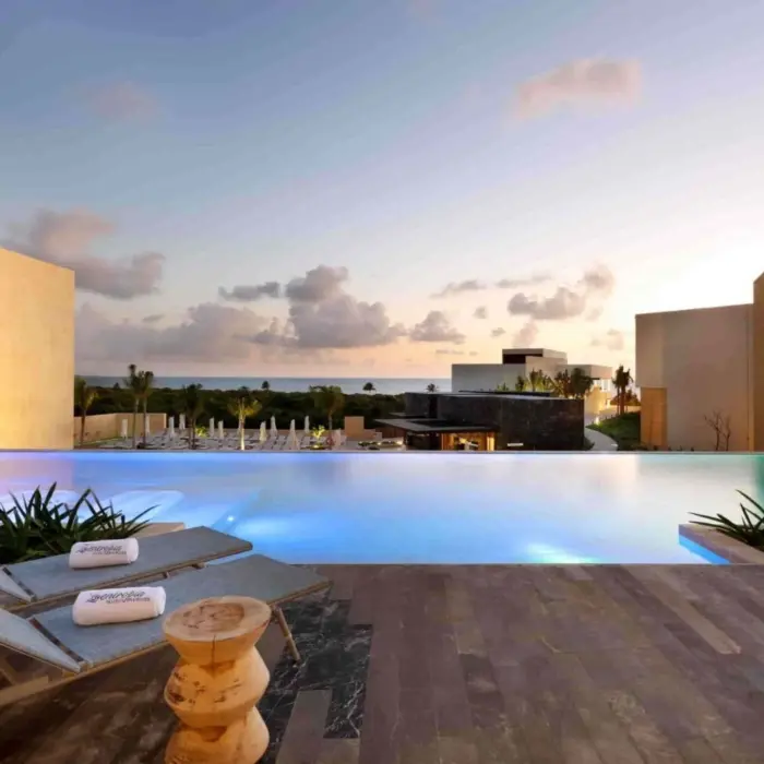 Infinity pool overlooking the ocean at sunset with lounge chairs at resort’s main pool area.