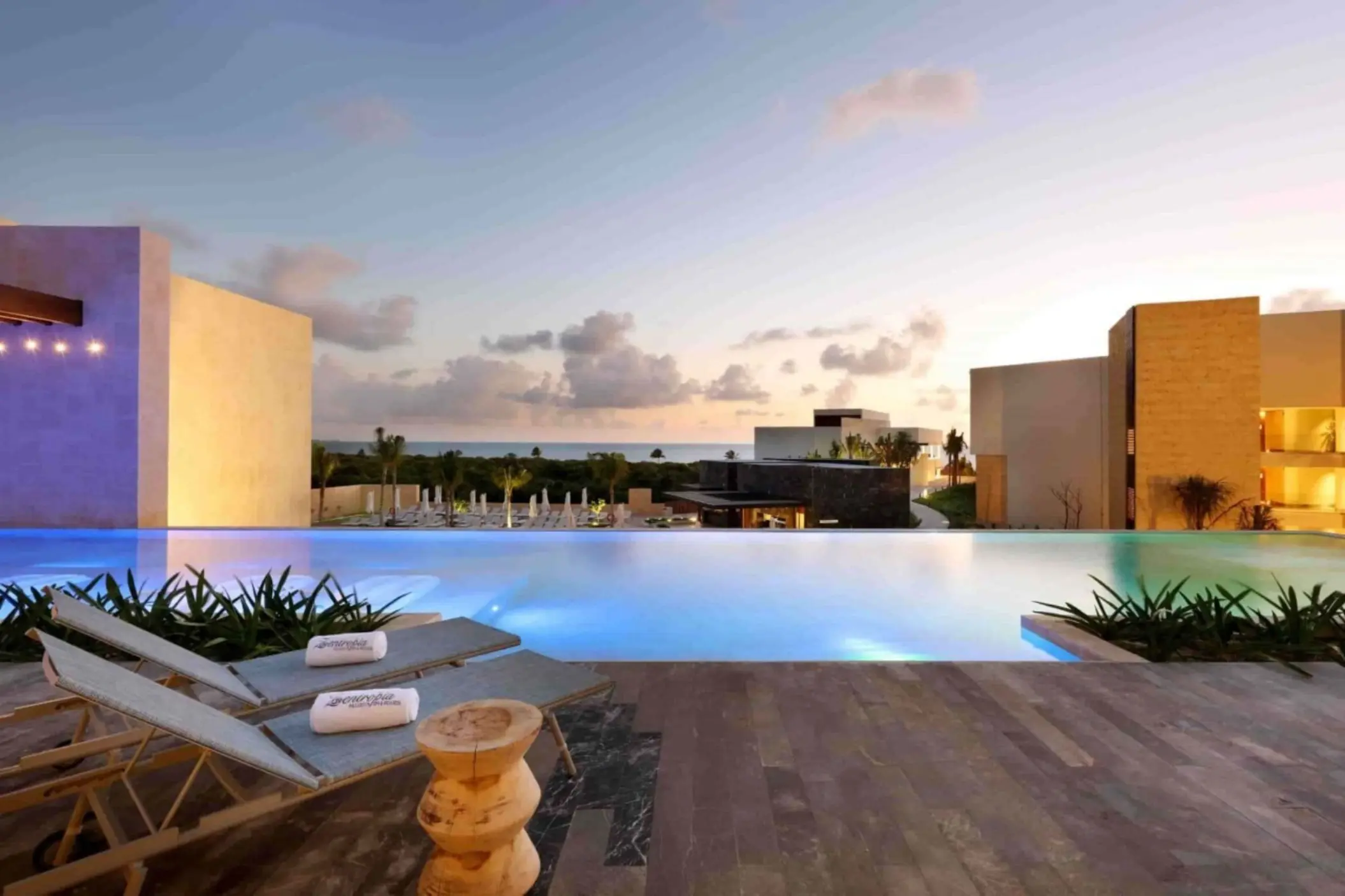 Infinity pool overlooking the ocean at sunset with lounge chairs at resort’s main pool area.