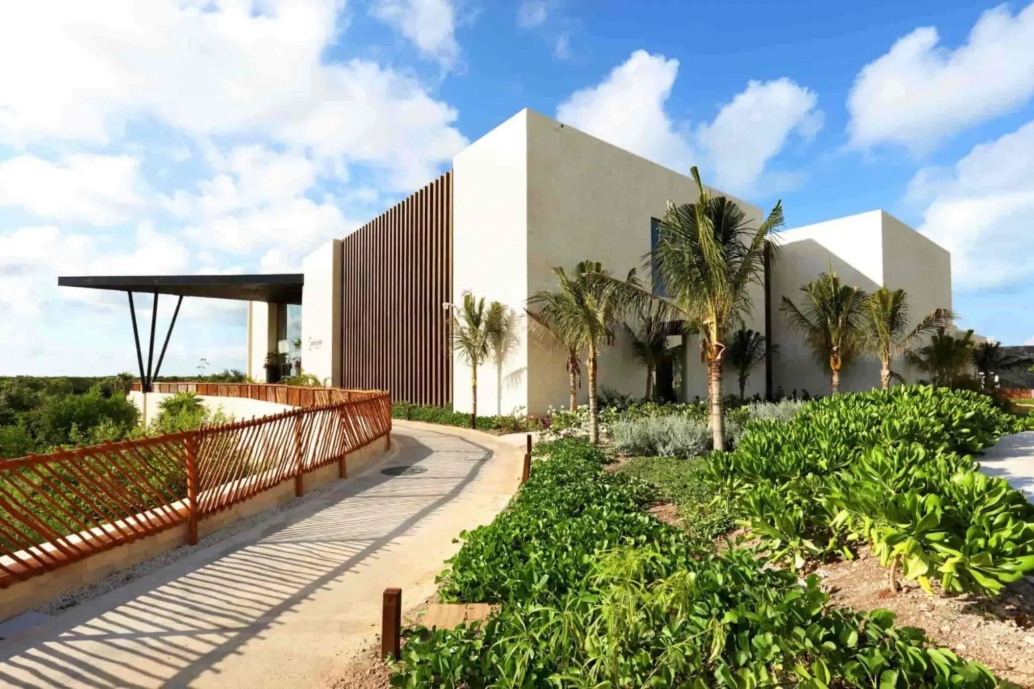 Modern building entrance surrounded by lush greenery and palm trees under a bright blue sky.