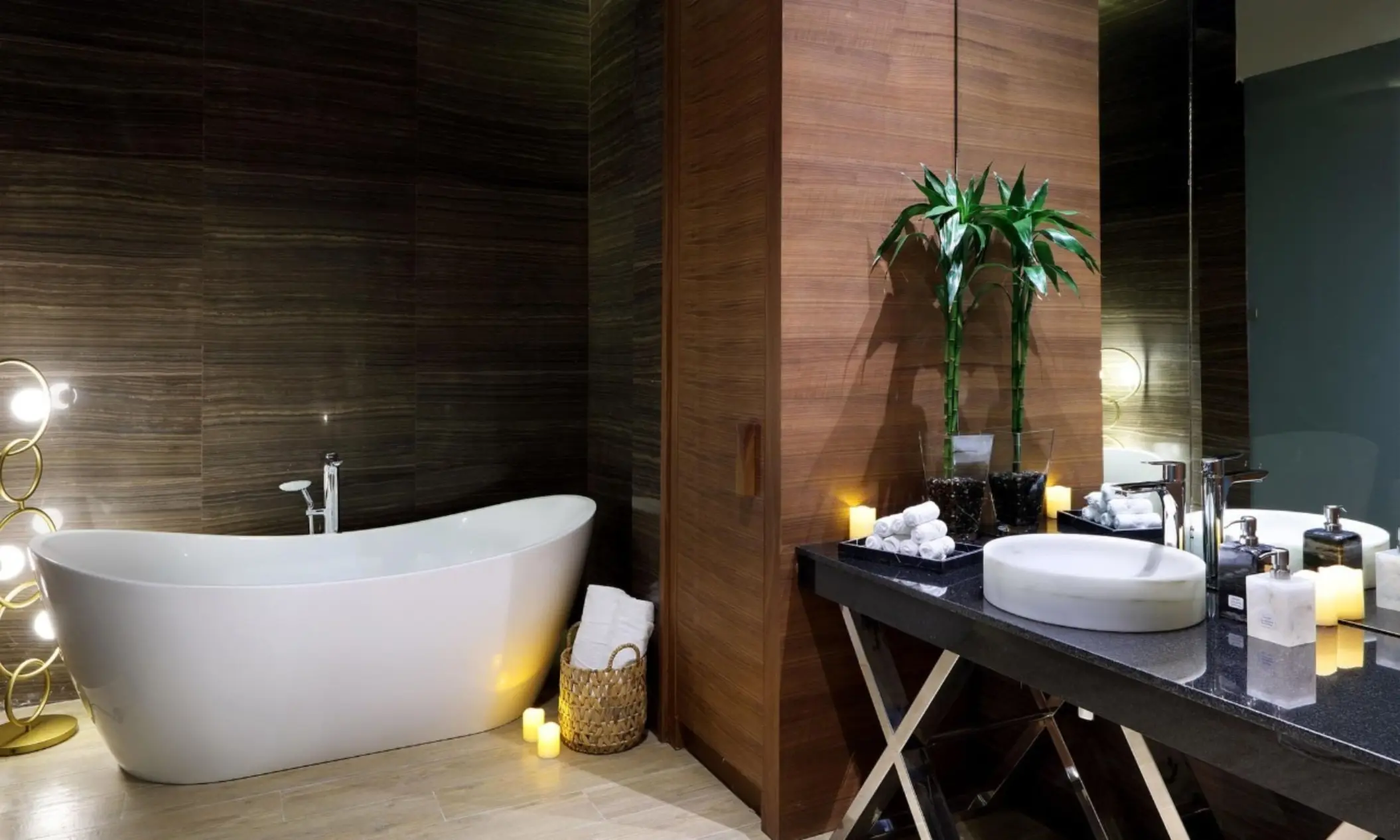 Elegant spa bathroom with a freestanding tub, dark wood walls, soft lighting, and a sleek vanity with candles.
