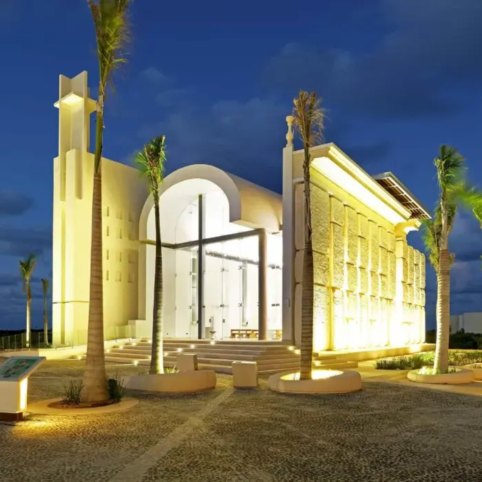 Grand illuminated chapel with tall palm trees and modern architectural design at twilight.
