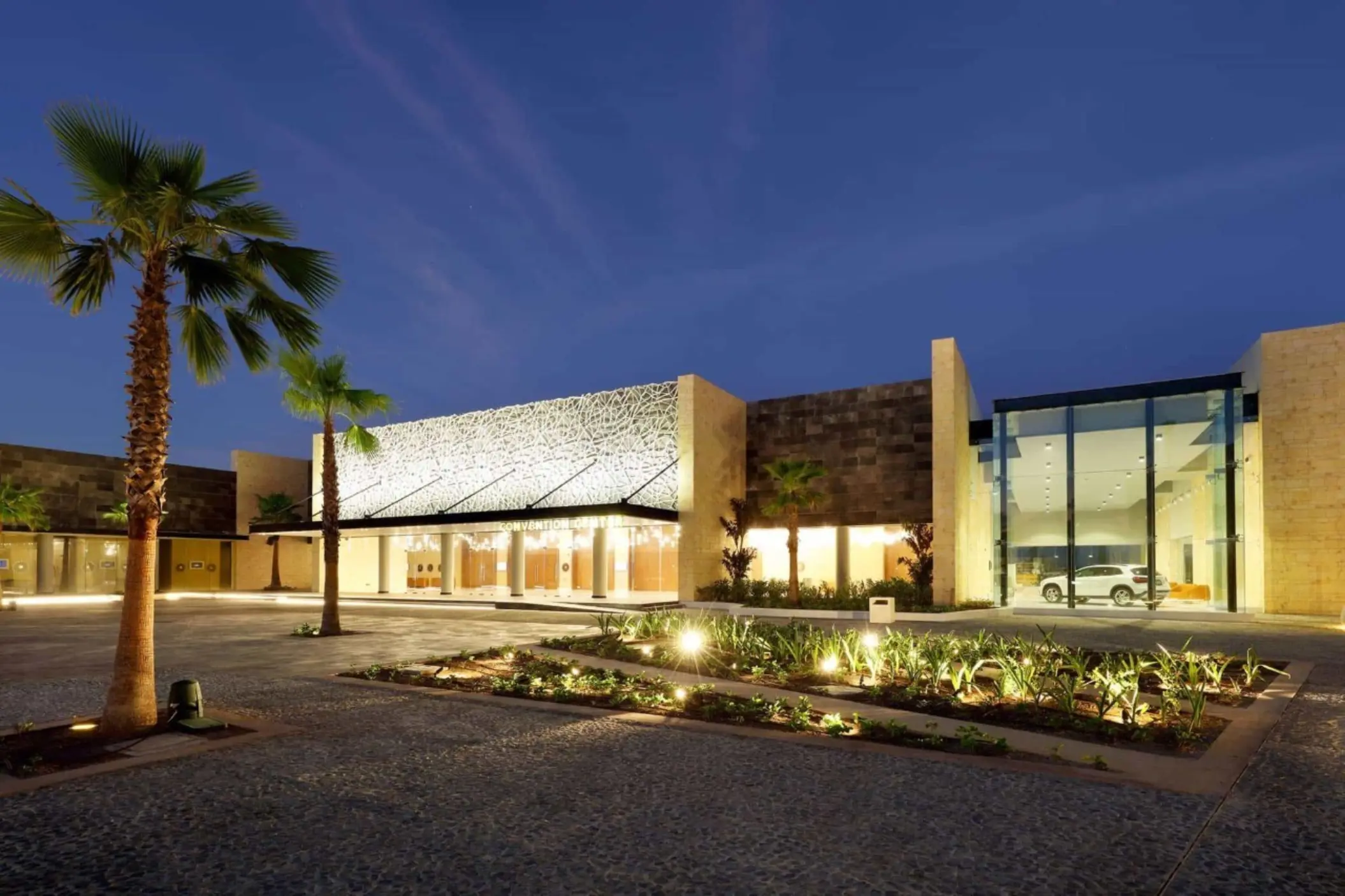 Night view of a modern resort convention center entrance with palm trees and warm lighting.