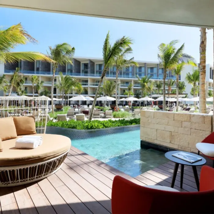 Swim-out suite patio with daybed and red chairs, overlooking tropical pool area and palm trees.