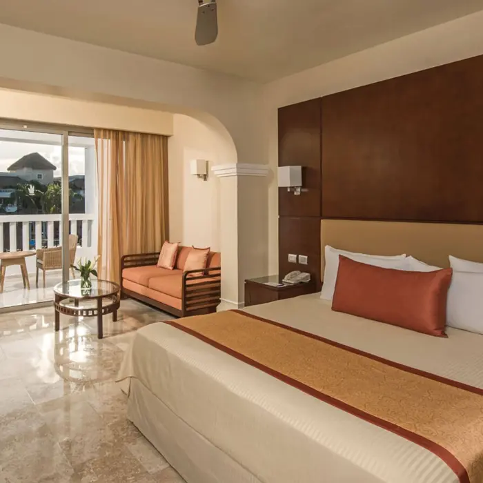 Elegant Junior Suite Deluxe at Grand Riviera Princess with a king-sized bed, sitting area, and balcony.