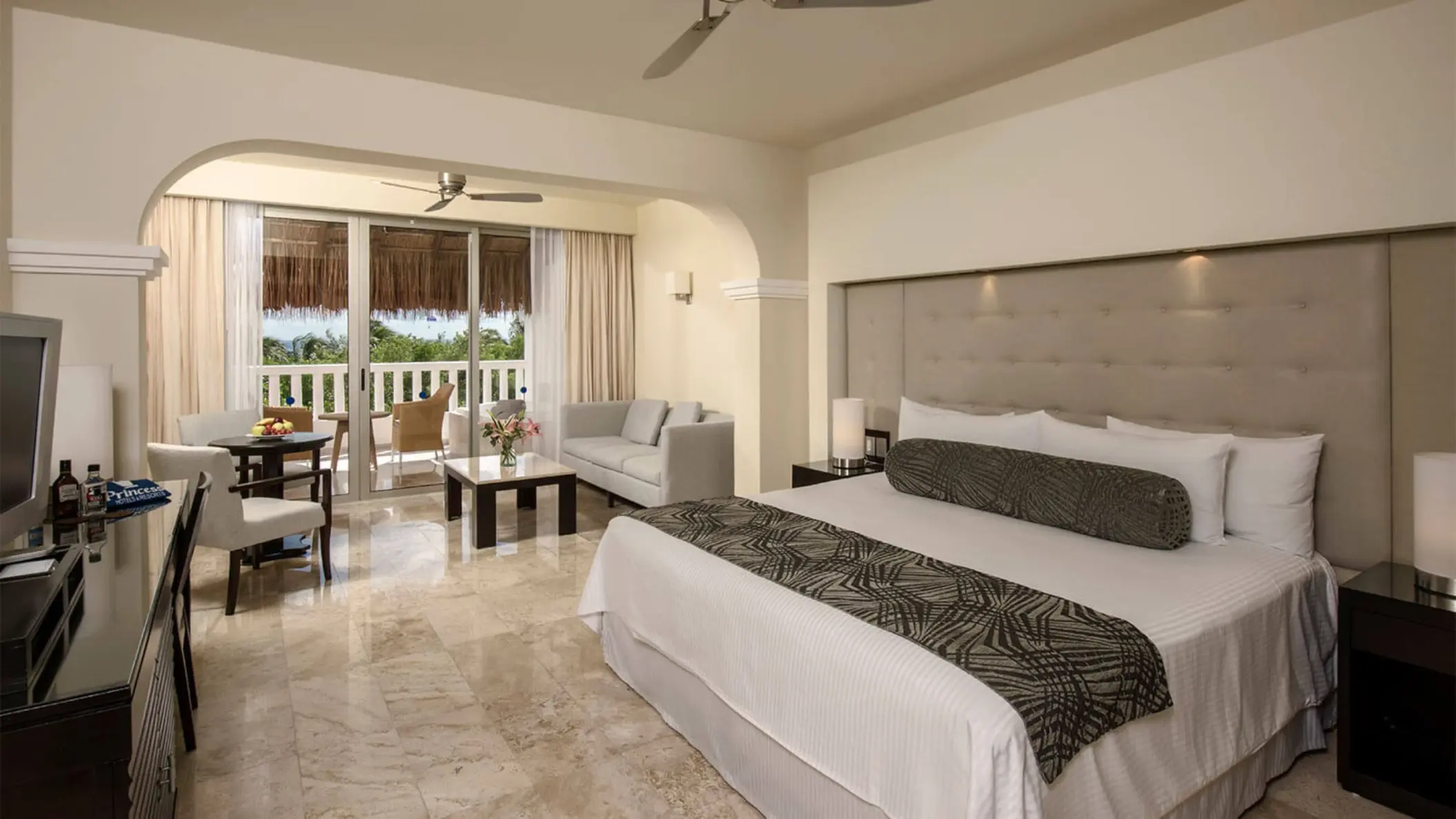 Spacious Platinum Suite at Grand Riviera Princess with a large bed, seating area, and balcony overlooking tropical foliage.