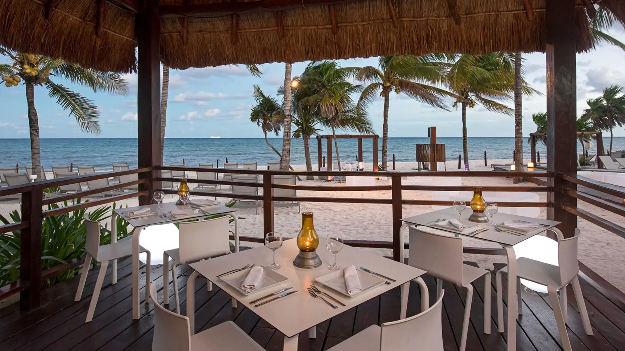 Charming oceanfront restaurant at Grand Riviera Princess with tables set under a thatched roof, offering stunning beach views.