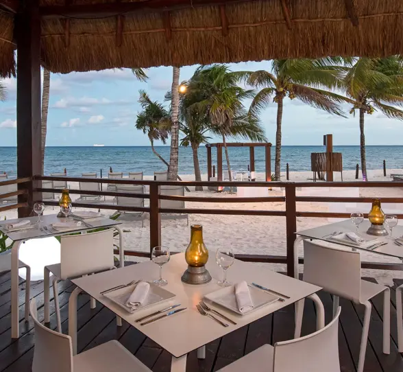Charming oceanfront restaurant at Grand Riviera Princess with tables set under a thatched roof, offering stunning beach views.