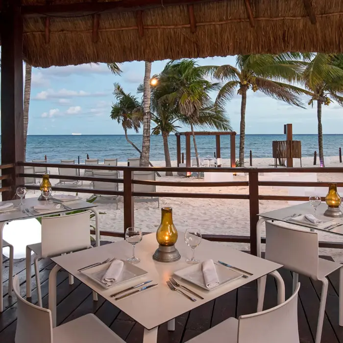 Charming oceanfront restaurant at Grand Riviera Princess with tables set under a thatched roof, offering stunning beach views.