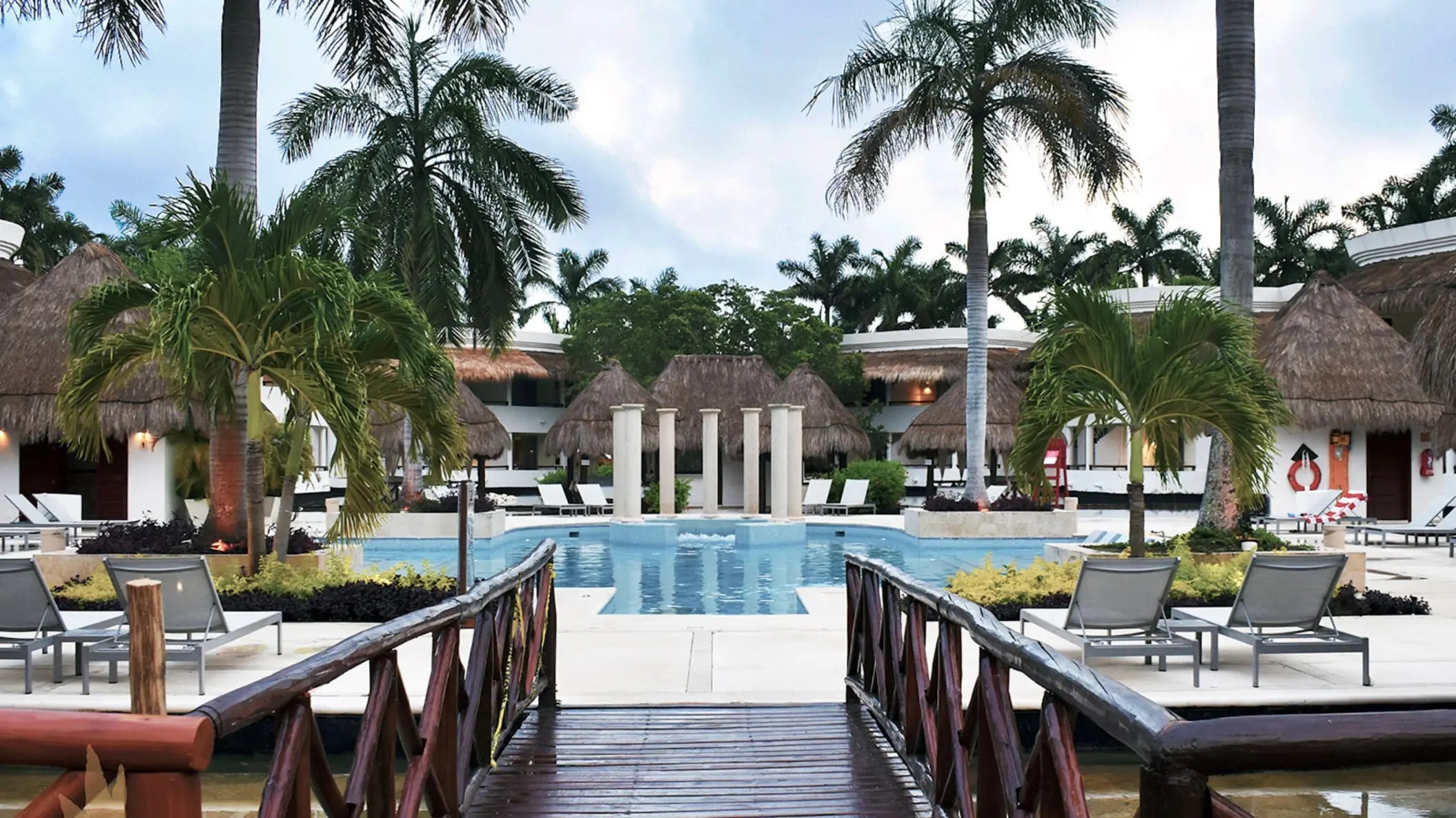 Serene pool area at Grand Riviera Princess with comfortable loungers, surrounded by lush palm trees and resort buildings.