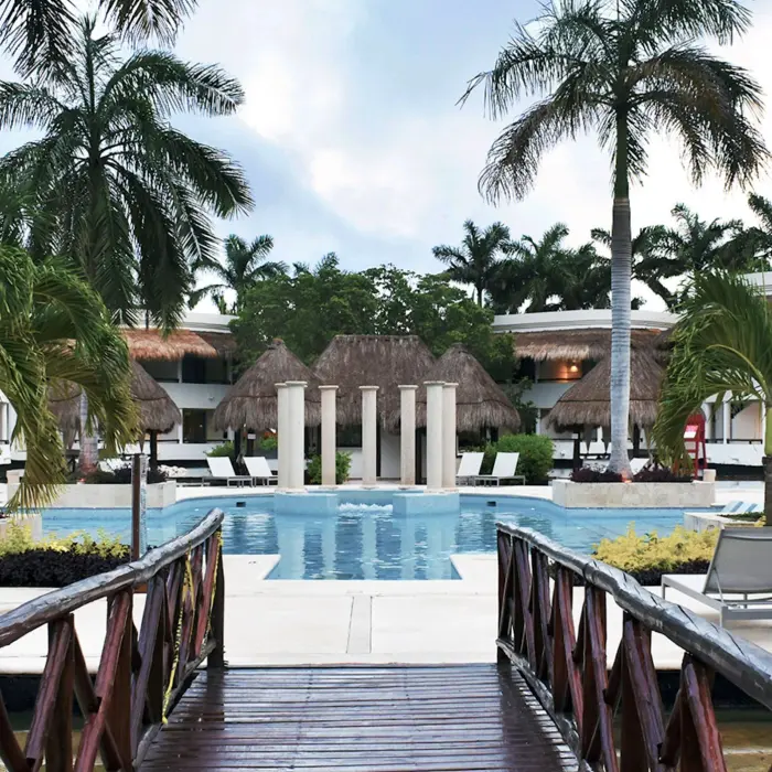 Serene pool area at Grand Riviera Princess with comfortable loungers, surrounded by lush palm trees and resort buildings.