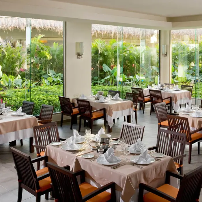 Bright and inviting interior of La Fondue restaurant at Grand Riviera Princess, with tables set and large windows overlooking greenery.