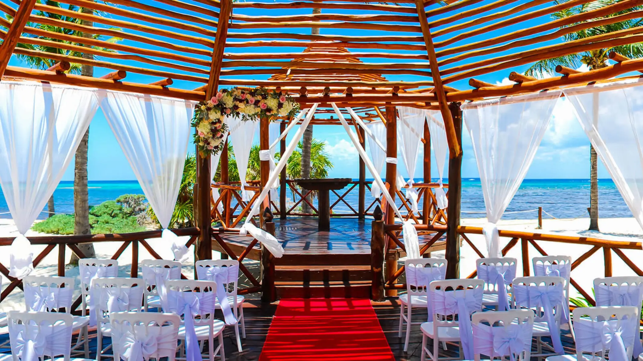 Beautiful beachside wedding gazebo at Grand Riviera Princess, decorated with flowers and white chairs, overlooking the ocean.