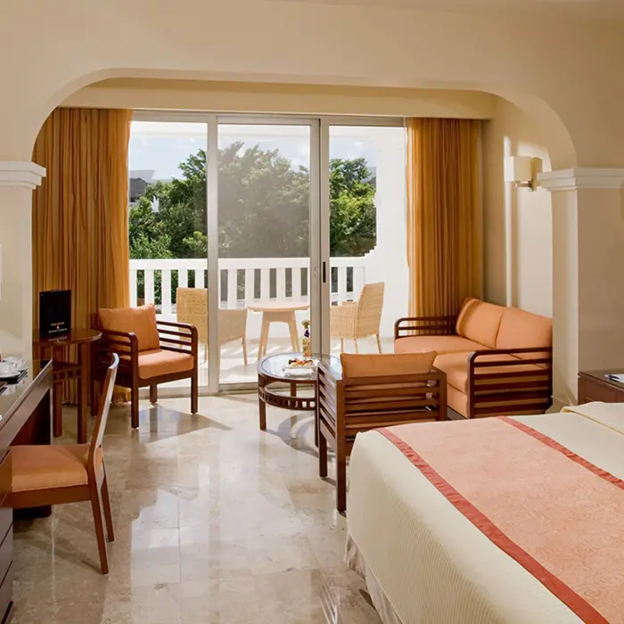 Bright suite at Grand Sunset Princess with a king bed, sitting area, desk, and a balcony with outdoor furniture.
