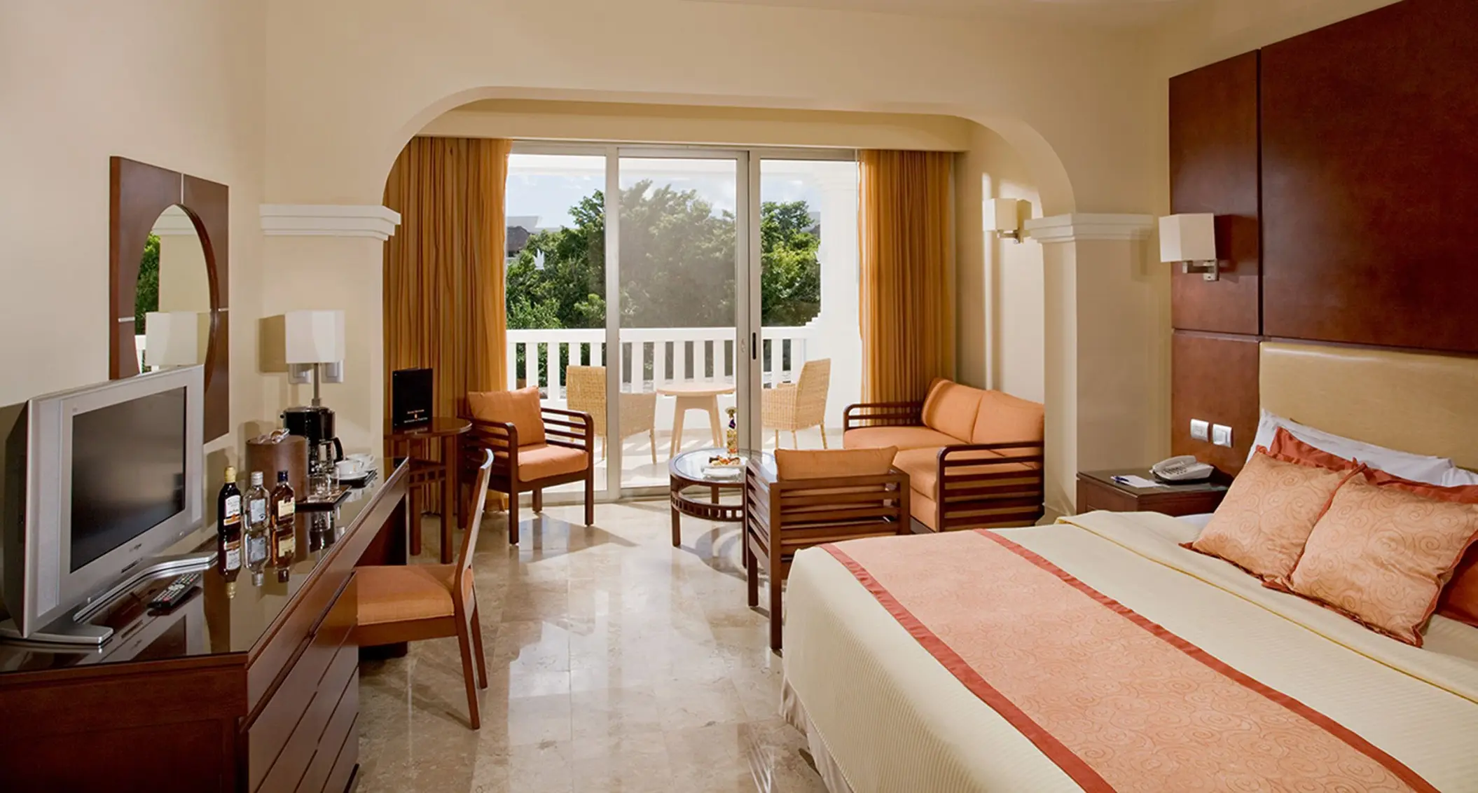 Bright suite at Grand Sunset Princess with a king bed, sitting area, desk, and a balcony with outdoor furniture.