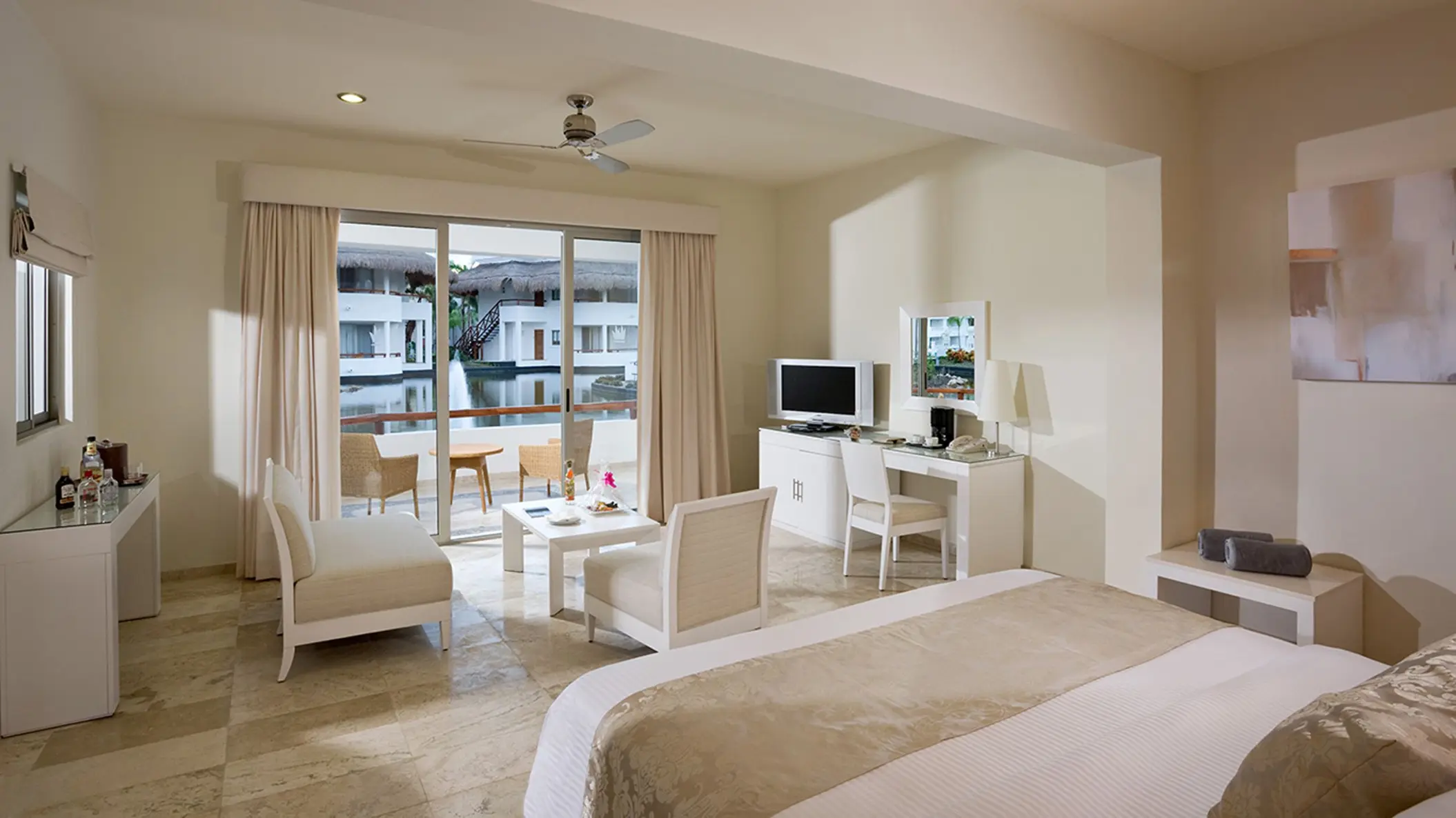Suite at Grand Sunset Princess with a king bed, living area, and balcony overlooking a serene water canal.