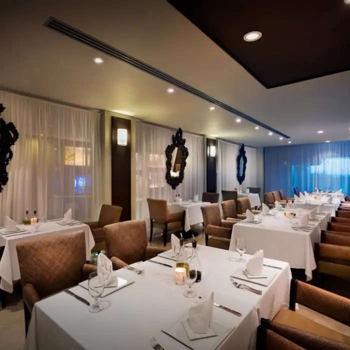 A formal dining room at Ciao Restaurant with white tablecloths, plush chairs, and ornate mirrors.