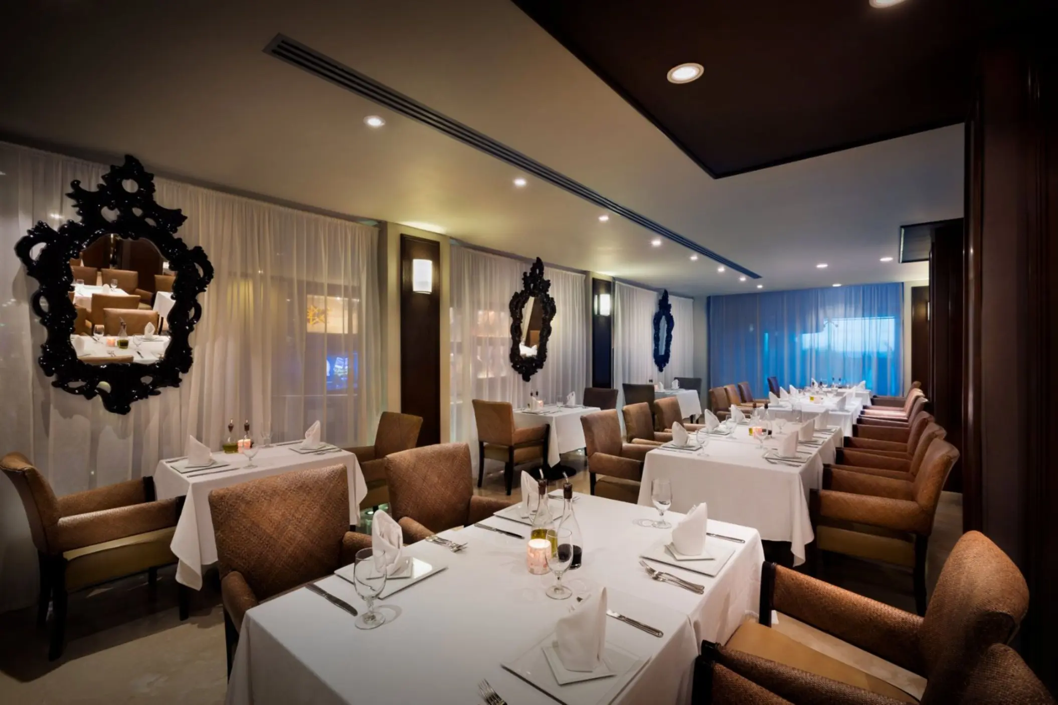 A formal dining room at Ciao Restaurant with white tablecloths, plush chairs, and ornate mirrors.
