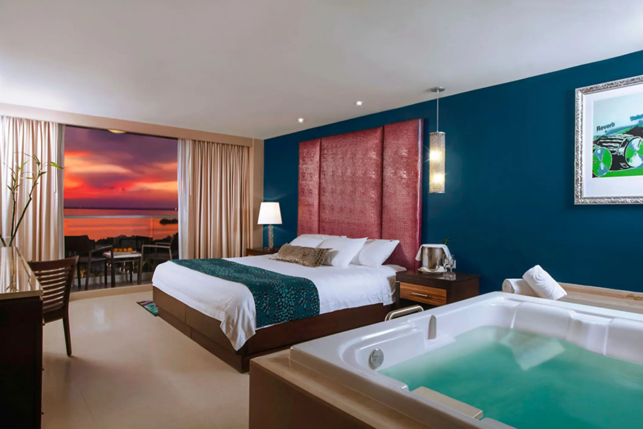 A modern hotel room with a king-sized bed, a jacuzzi, and a balcony with a sunset view.