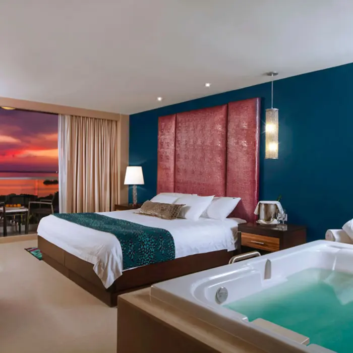 A modern hotel room with a king-sized bed, a jacuzzi, and a balcony with a sunset view.