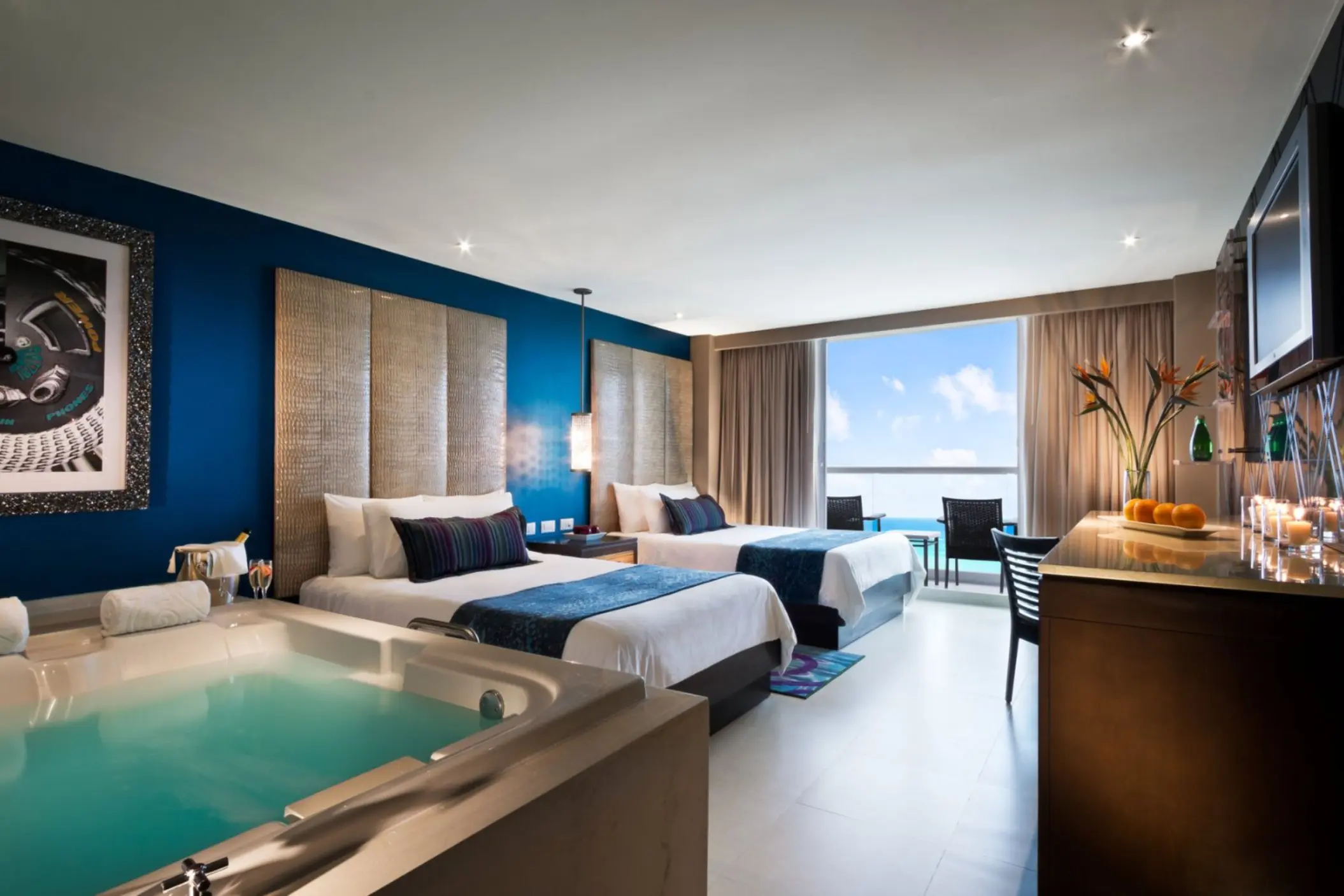 A spacious hotel room with two beds, a large jacuzzi, and a balcony overlooking the ocean.