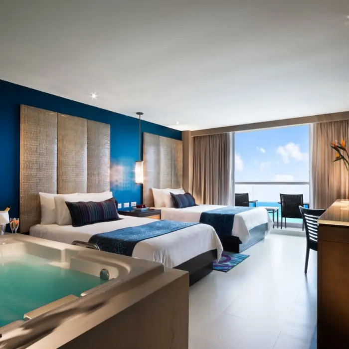 A spacious hotel room with two beds, a large jacuzzi, and a balcony overlooking the ocean.