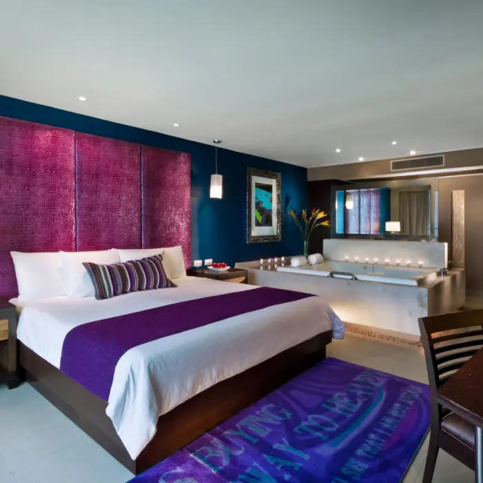 A stylish hotel suite with a king-sized bed, a jacuzzi tub, and modern decor with bold colors.