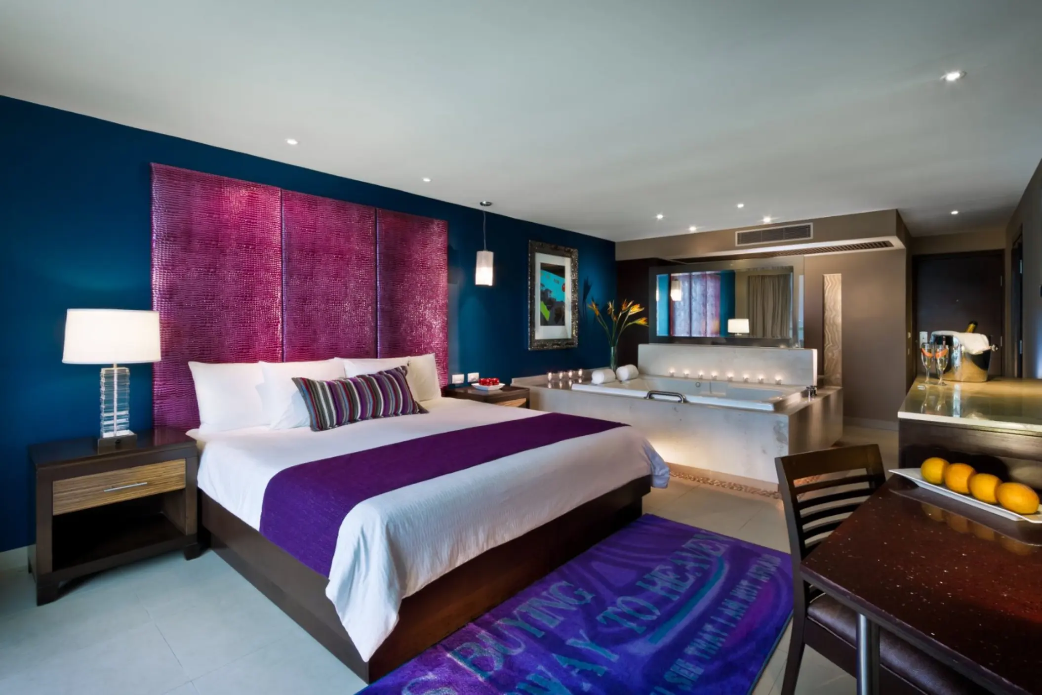 A stylish hotel suite with a king-sized bed, a jacuzzi tub, and modern decor with bold colors.