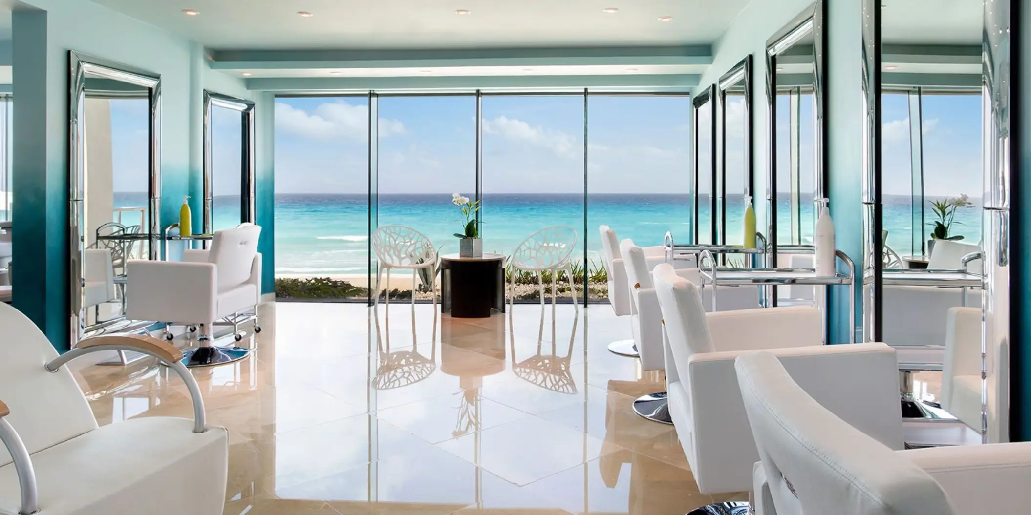 A bright, modern hair salon with multiple stations and a floor-to-ceiling window view of the beach.