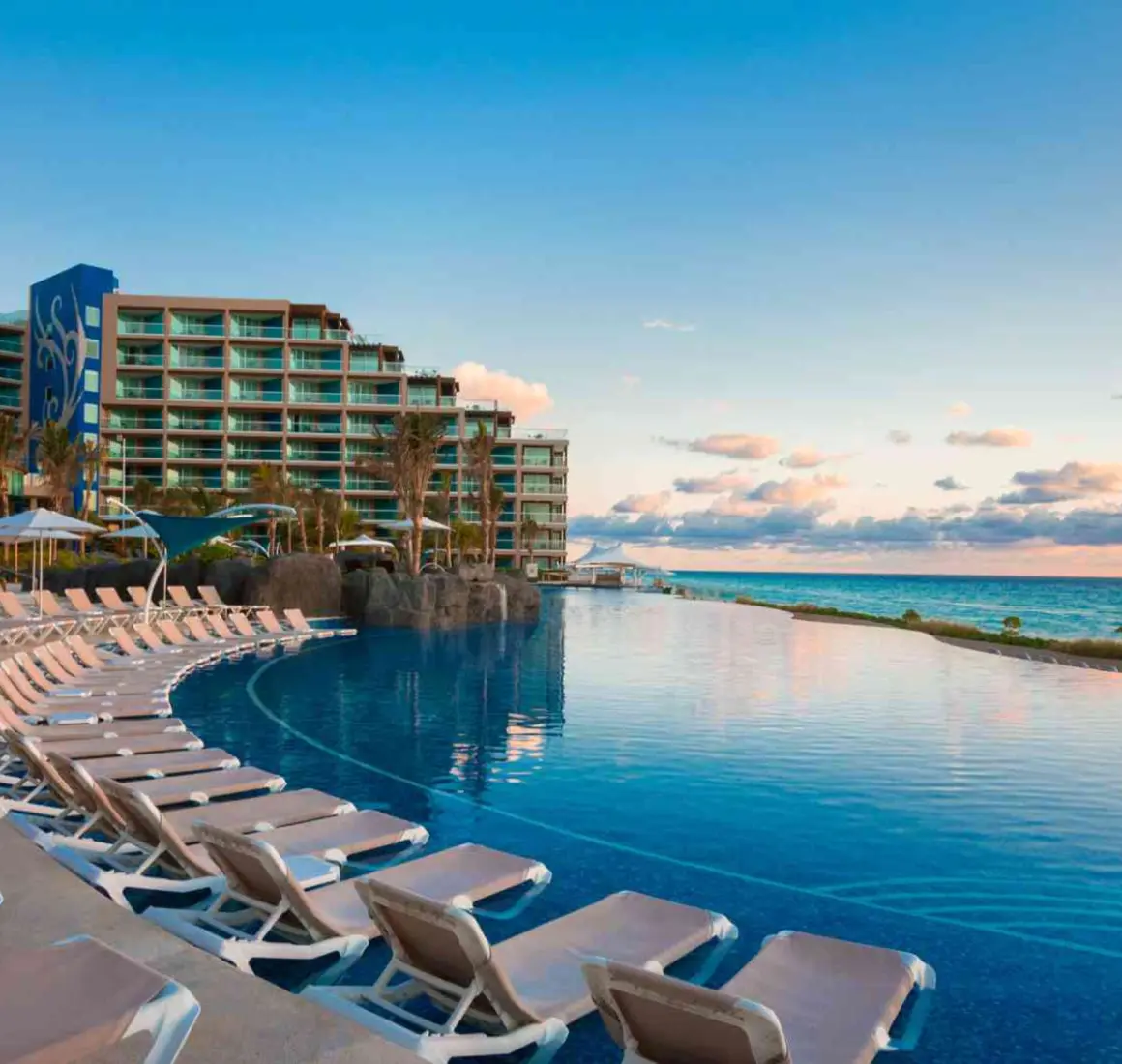 An expansive infinity pool with a row of lounge chairs and a view of the beach and resort building.