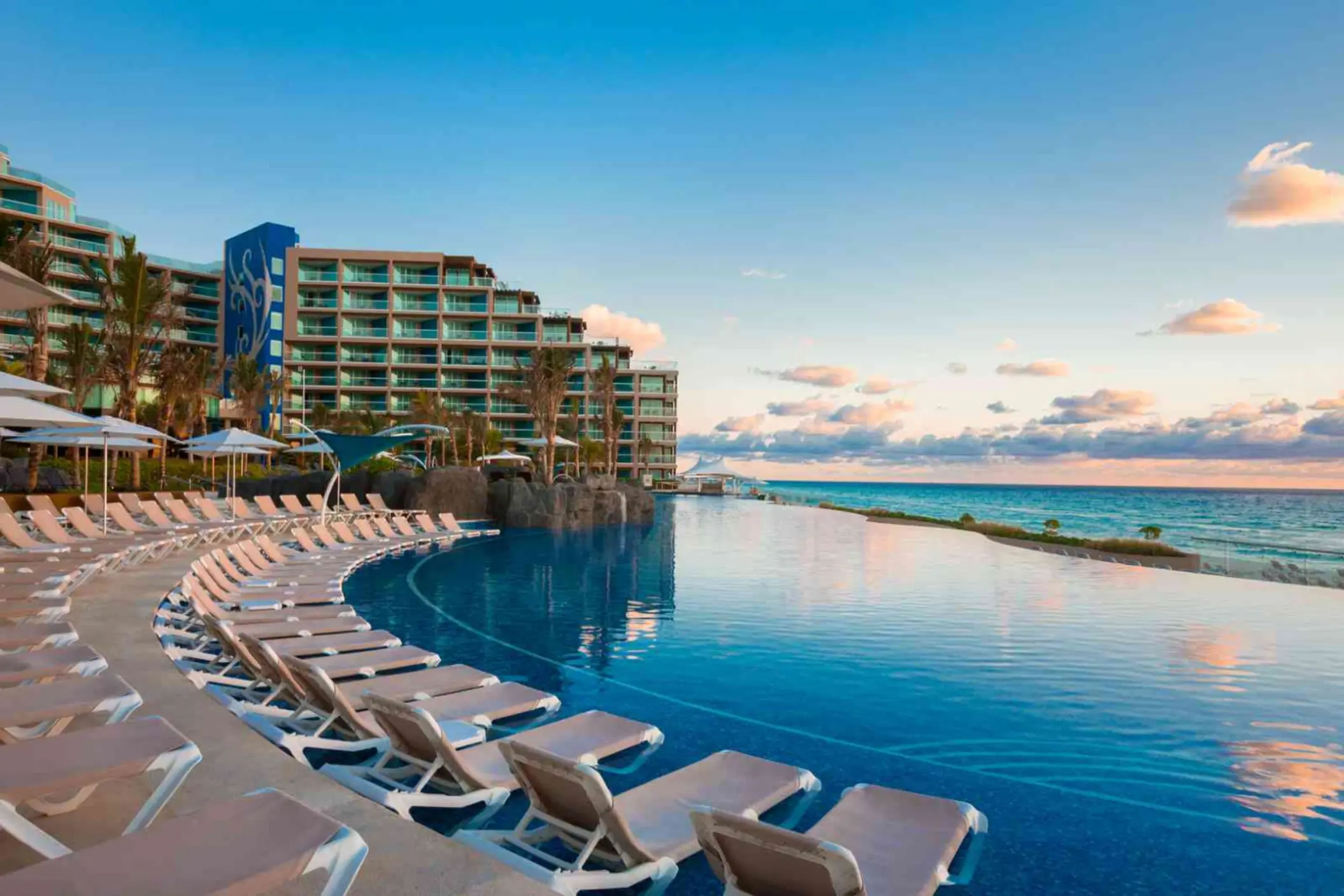 An expansive infinity pool with a row of lounge chairs and a view of the beach and resort building.