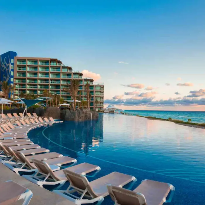 An expansive infinity pool with a row of lounge chairs and a view of the beach and resort building.