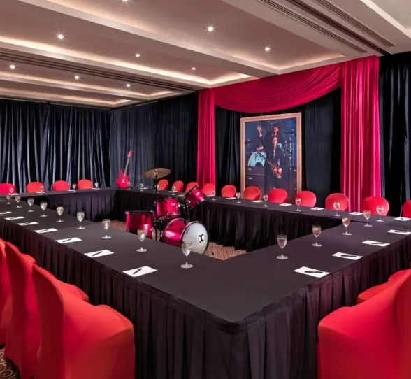 A U-shaped meeting room with black tablecloths, red chairs, and music-themed decor including a drum set.